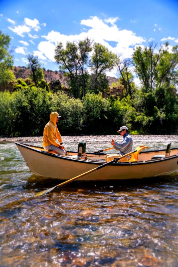 Colorado fly fishing guide rowing a drift boat with angler on a clear river