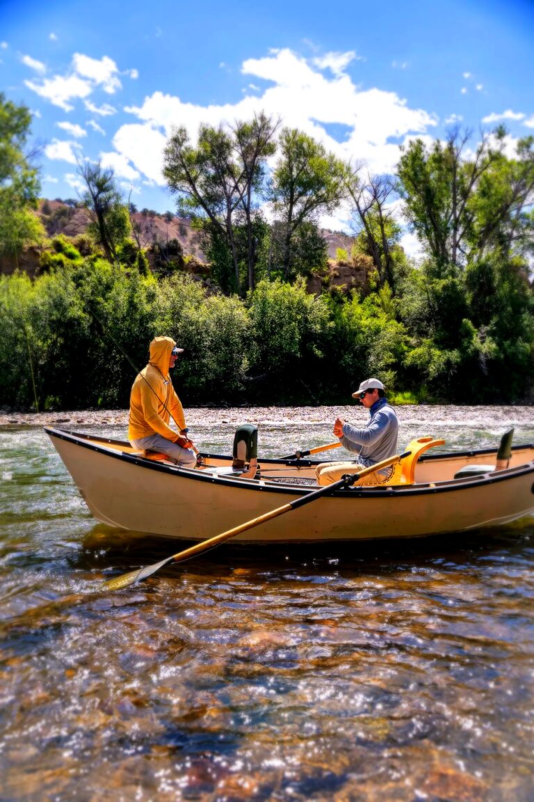 Colorado fly fishing guide rowing a drift boat with angler on a clear river