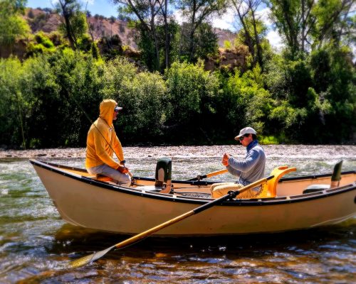 Colorado fly fishing guide rowing a drift boat with angler on a clear river