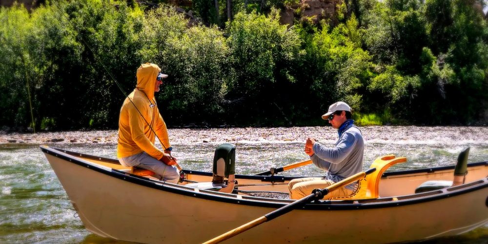 Colorado fly fishing guide rowing a drift boat with angler on a clear river